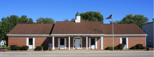 A brick building with a peaked roof, featuring a flagpole and sign for the J.C. Penney Memorial Library-Museum.