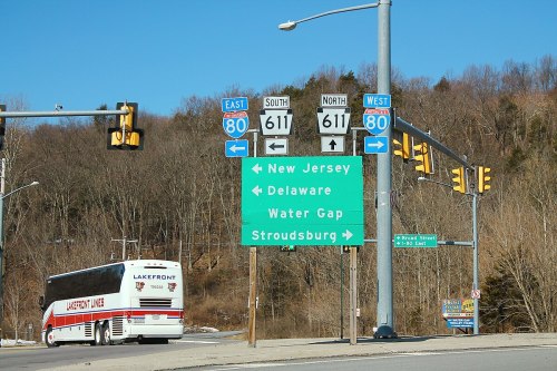 Road sign directing traffic towards New Jersey, Delaware, Water Gap, and Stroudsburg, with a bus in the foreground.
