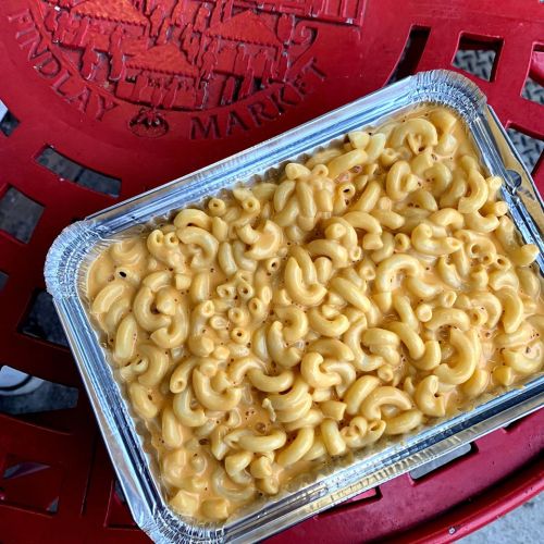 A foil tray filled with creamy macaroni and cheese, resting on a red outdoor chair.