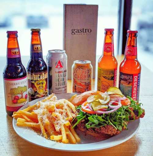 A plate of fries and a burger topped with veggies, surrounded by various craft beers and a menu on a wooden table.