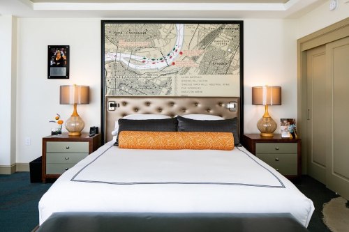 A modern hotel room featuring a large bed, decorative pillows, lamps, and a map artwork above the headboard.