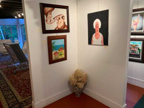 Art gallery corner featuring two framed paintings and a vase of dried flowers on the floor.