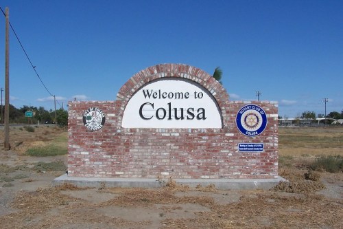 Welcome sign for Colusa, California, featuring brick design and local symbols against a clear blue sky.