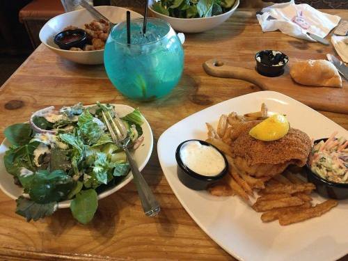 A plate with fried fish and fries, a salad, and a blue drink on a wooden table.