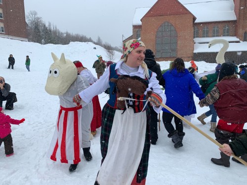 A snowy scene with people in costumes, including a horse head and traditional attire, celebrating outdoors.