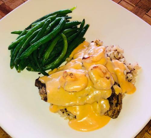 A plate featuring grilled fish topped with creamy sauce, served over rice and accompanied by green beans.