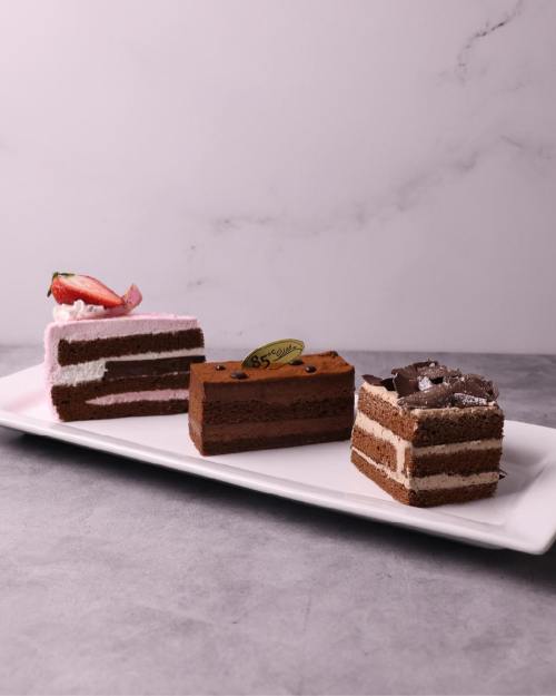 Three layers of chocolate cake on a white platter, featuring pink frosting and a strawberry on one slice.