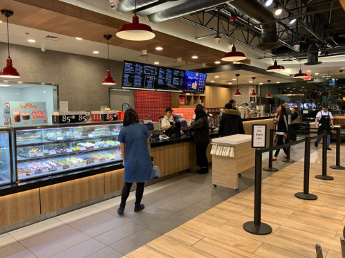 A busy café with a display case of pastries, customers at the counter, and a menu board overhead.