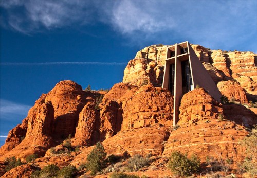 A modern building perched on a red rock formation under a blue sky with wispy clouds.