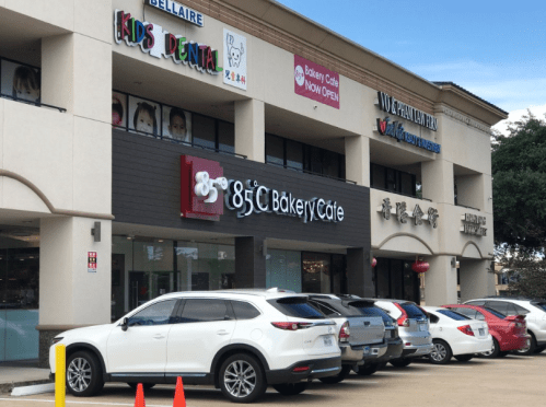 A storefront featuring G&C Bakery Café, with nearby dental and other businesses, and parked cars in front.