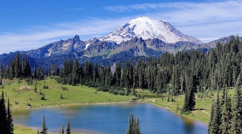 A serene landscape featuring a clear lake surrounded by lush greenery, with a snow-capped mountain in the background.