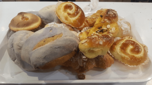 A variety of baked goods on a white platter, including rolls, pastries, and sweet breads.