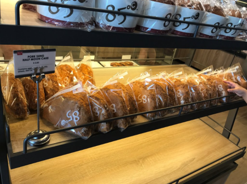 A display of packaged pork sung half moon cakes on a wooden shelf, with a price sign in front.