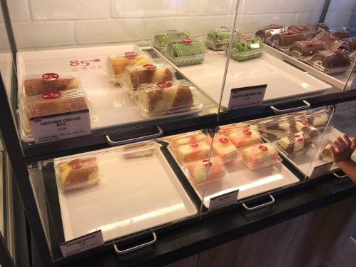 Display case with various desserts in clear containers, including coconut custard and matcha options, with price tags.
