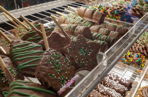 A display of chocolate-covered treats on sticks, decorated with sprinkles and colorful candies.