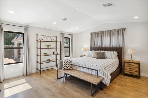 Bright, modern bedroom featuring a large bed, wooden bench, and stylish decor with natural light from windows.