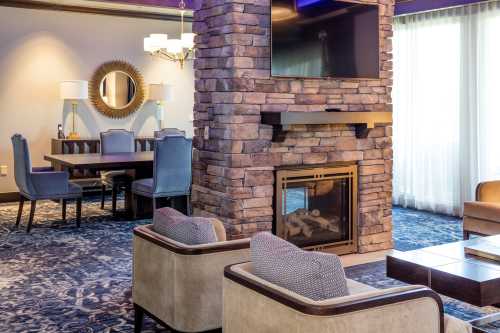 Cozy living area featuring a stone fireplace, TV, dining table, and comfortable seating with large windows.