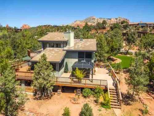 A spacious two-story house surrounded by trees, with a large deck and scenic mountain views in the background.