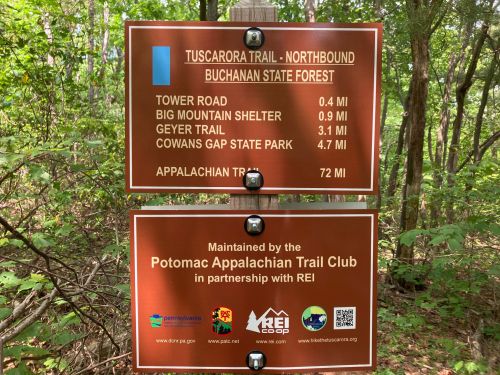 Signpost in a forest displaying trail distances to various locations, including Cowans Gap State Park and Big Mountain Shelter.