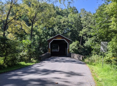 A scenic view of a covered bridge surrounded by lush greenery and trees on a sunny day.