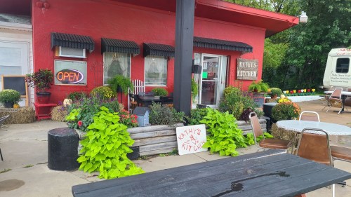 A vibrant red building with "Kathy's Kitchen" sign, surrounded by colorful plants and outdoor seating.