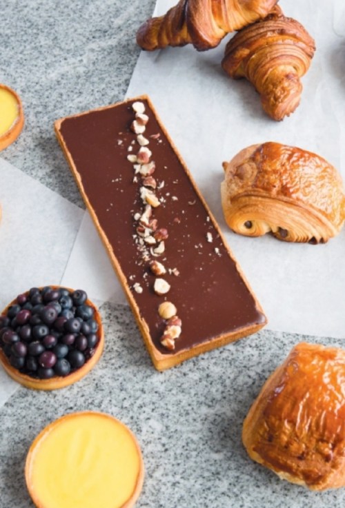 A variety of pastries and desserts, including chocolate tart, croissants, and blueberry tarts on a marble surface.