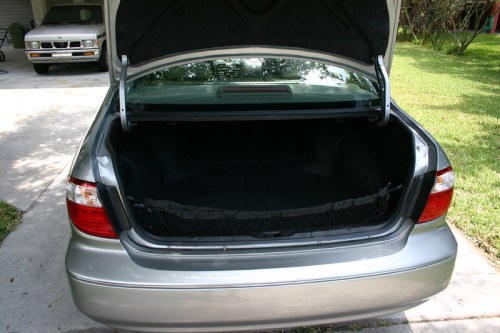 An open car trunk showing a spacious interior, parked on a driveway with grass in the background.