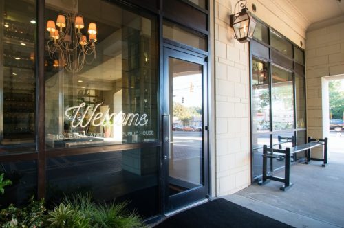 Entrance of a public house with a "Welcome" sign, large windows, and outdoor seating area.