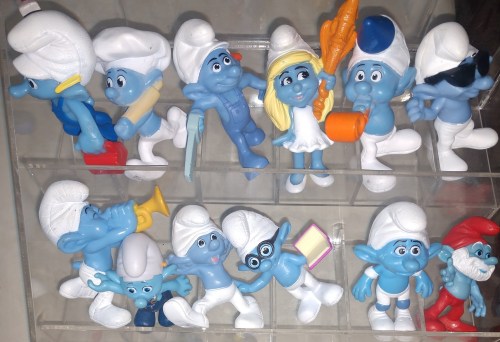 A collection of colorful Smurf figurines in various poses, displayed in a clear container.