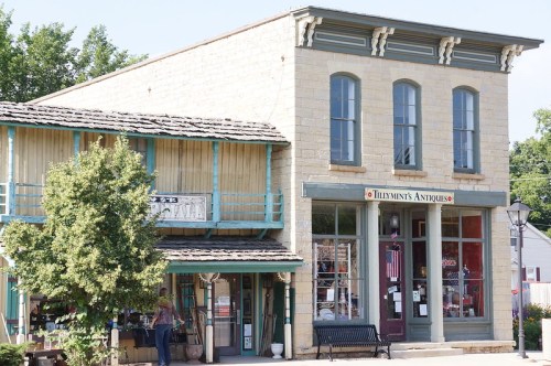 A charming antique shop with a stone facade, blue accents, and a welcoming entrance in a quaint town setting.