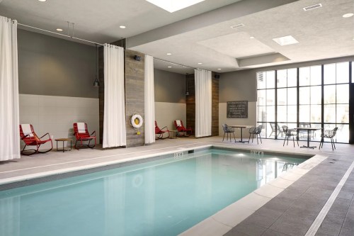 Indoor swimming pool area with red lounge chairs, white curtains, and a large window letting in natural light.