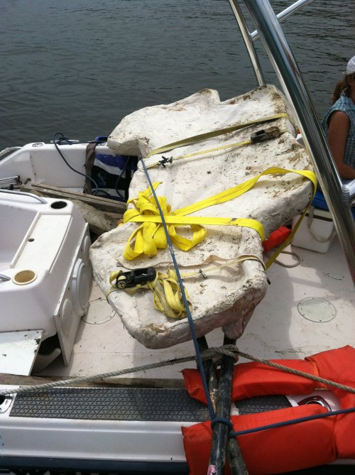 A large, white object secured with yellow straps on a boat, with life jackets and equipment visible in the background.