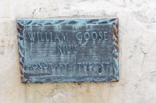 Bronze plaque reading "William Goose, NIU's Honorary Student," mounted on a textured stone wall.
