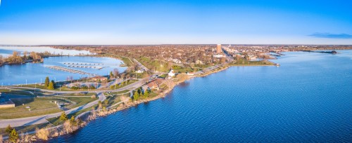 Aerial view of a serene waterfront with parks, docks, and a small town along the shore under a clear blue sky.
