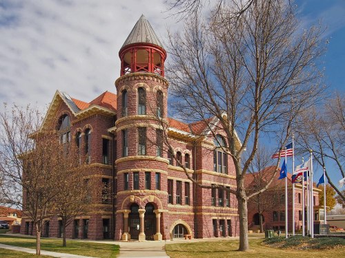 Historic brick building with a turret, surrounded by trees and flags, under a partly cloudy sky.