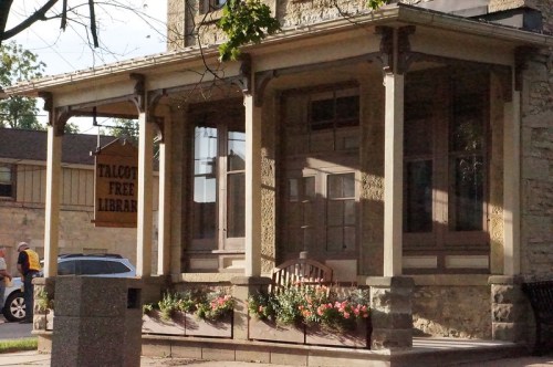 Historic building with a sign reading "Talcott Free Library," featuring a porch and flower planters.