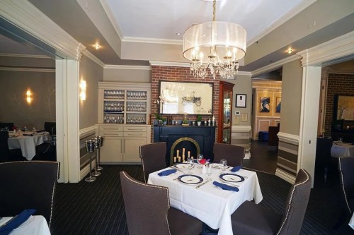 Elegant restaurant interior featuring a chandelier, neatly set tables, and a cozy fireplace.