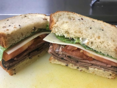 A close-up of a sandwich with layers of roast beef, cheese, lettuce, and tomato, served on seeded bread.