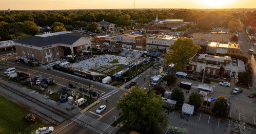 Aerial view of a lively outdoor event with tents, people, and sunset over a town square.