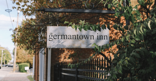 Sign for "The Germantown Inn" surrounded by greenery, with a brick wall in the background.