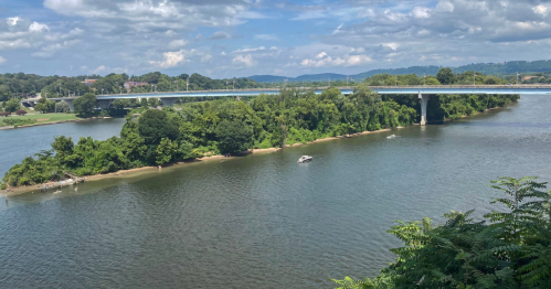 A scenic view of a river with lush greenery and a bridge in the background under a partly cloudy sky.