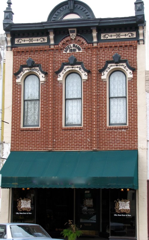 Historic brick building with decorative windows and a green awning, featuring intricate architectural details.