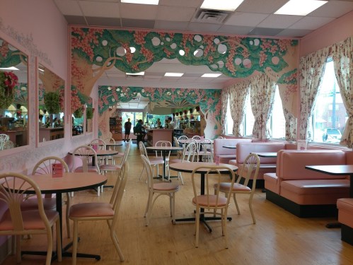 A pastel-colored café interior with pink booths, floral wallpaper, and large windows, creating a bright, inviting atmosphere.