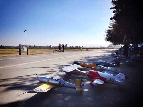 A row of model airplanes lined up on a runway under a clear blue sky, with trees in the background.