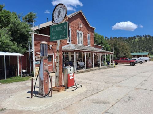 Historic building in Aladdin, Wyoming, with vintage gas pumps and a sign showing elevation and population.