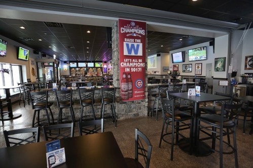 A spacious sports bar with empty tables, screens showing games, and a banner celebrating a championship win.