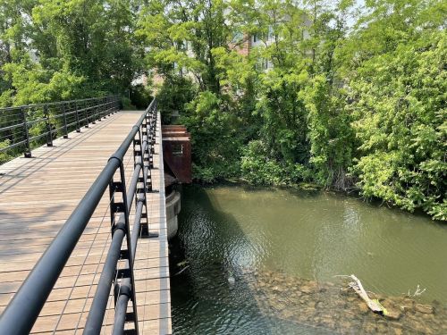 A wooden bridge spans a calm river, surrounded by lush green trees and foliage.