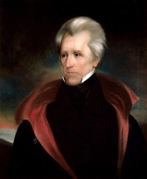 Portrait of a man with white hair and a dark coat, set against a moody background.