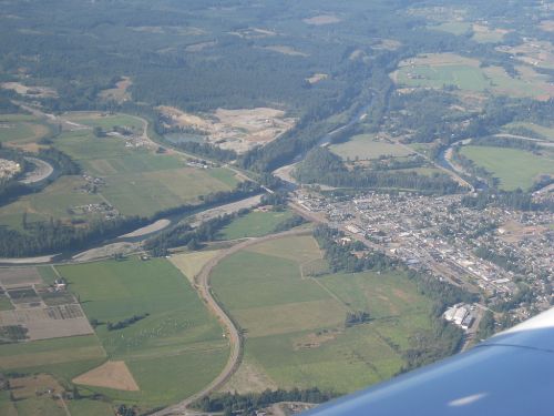 Aerial view of green fields, winding rivers, and a small town surrounded by trees and hills.