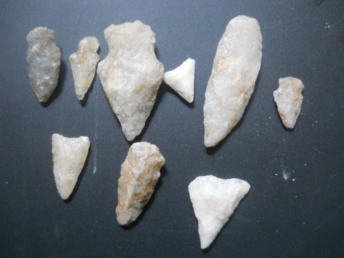 A collection of various stone tools and arrowheads arranged on a dark surface.